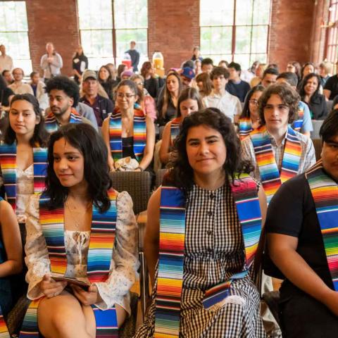 Seated people at ceremony smiling and wearing multicolored stoles.