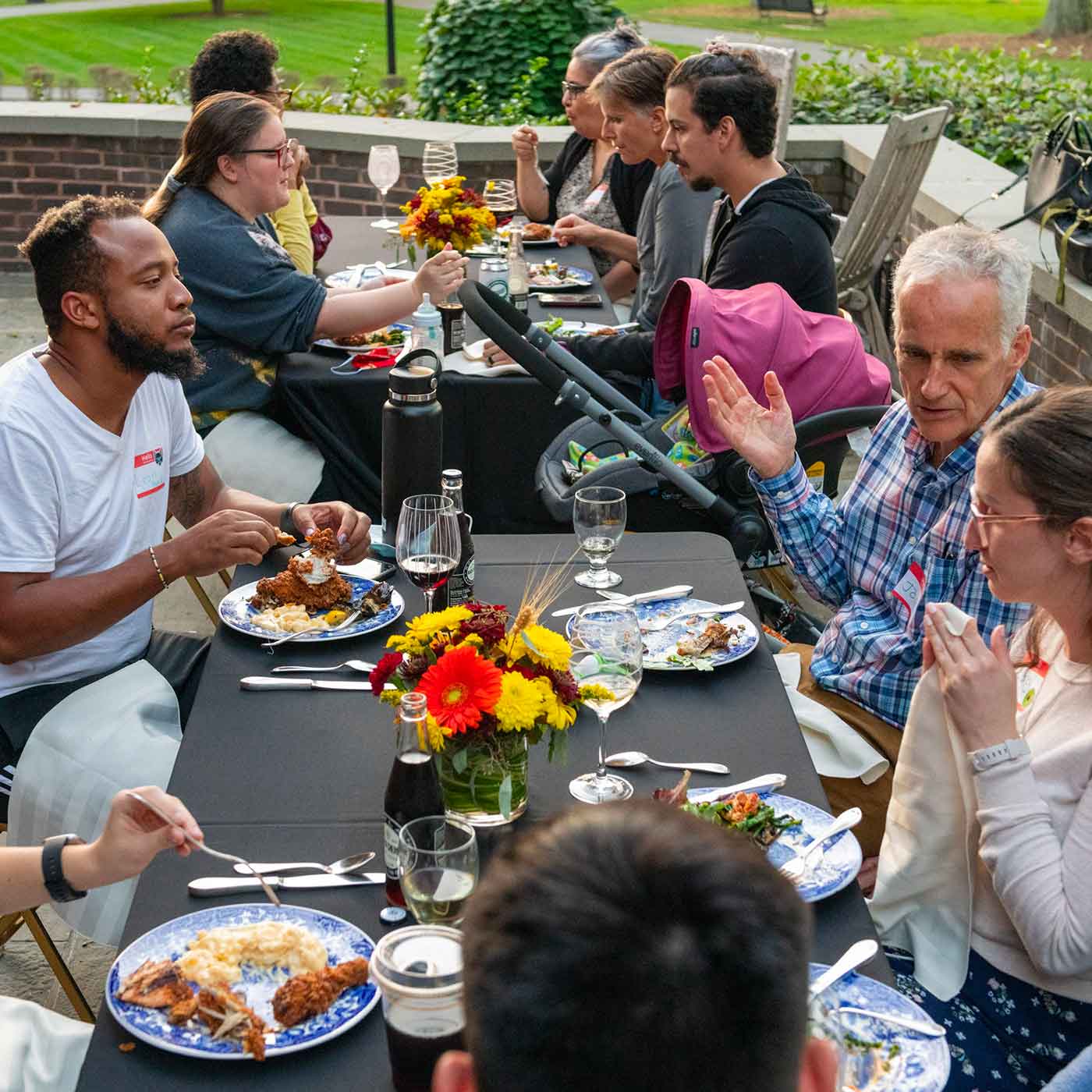 A group of people sit around an outdoor table with plates of food in front of them