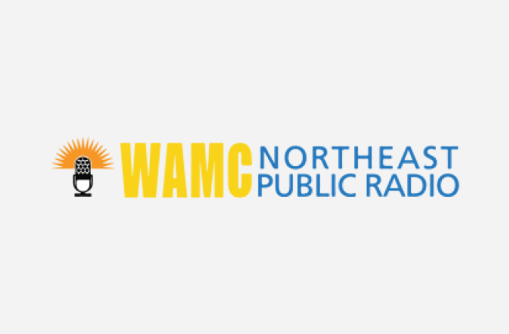 The WAMC logo, with an illustration of a microphone, followed by the letters WAMG in block yellow font, and the words Northeast Public Radio in blue.
