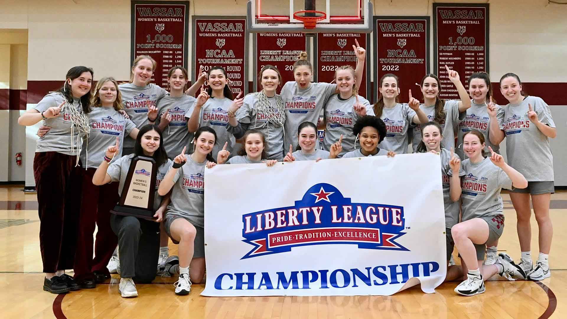 Baskeball team smiling and holding up a Liberty League Championship banner.