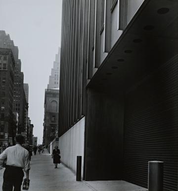 Seagram Building, New York City, showing the sidewalk with some people and surrounding buildings, in black and white.
