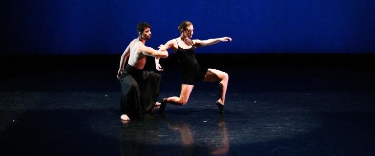 Two dancers perform on a darkened stage.