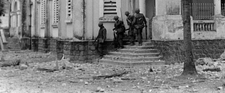 Black and white photo of a group of soldiers leaving a shelled building