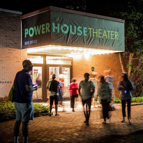 People standing in front of the entrance of the Powerhouse theater at night.