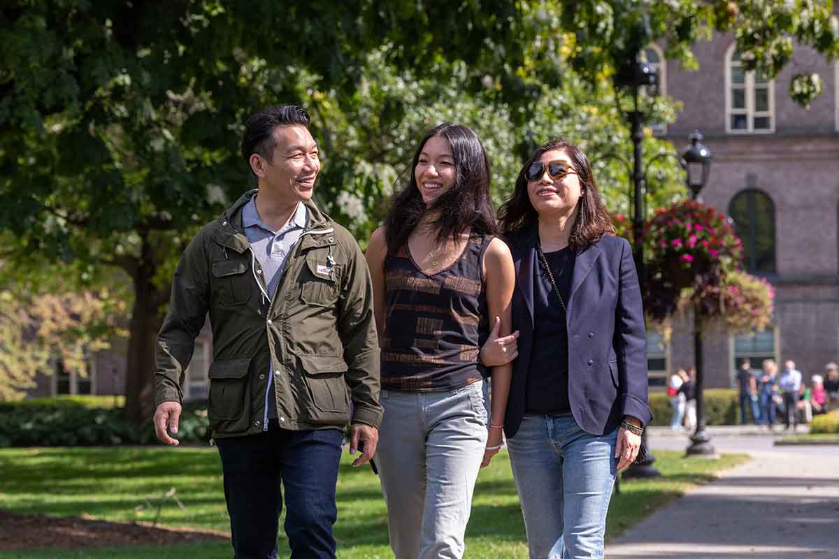 A family of three people walking in front of Main Building, smiling