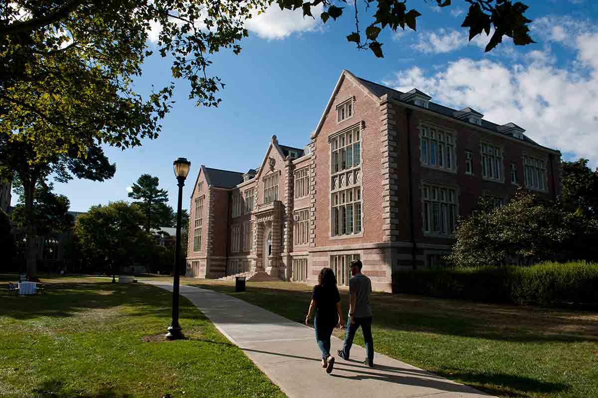 Two people walking on a path in front of Rockefeller Hall