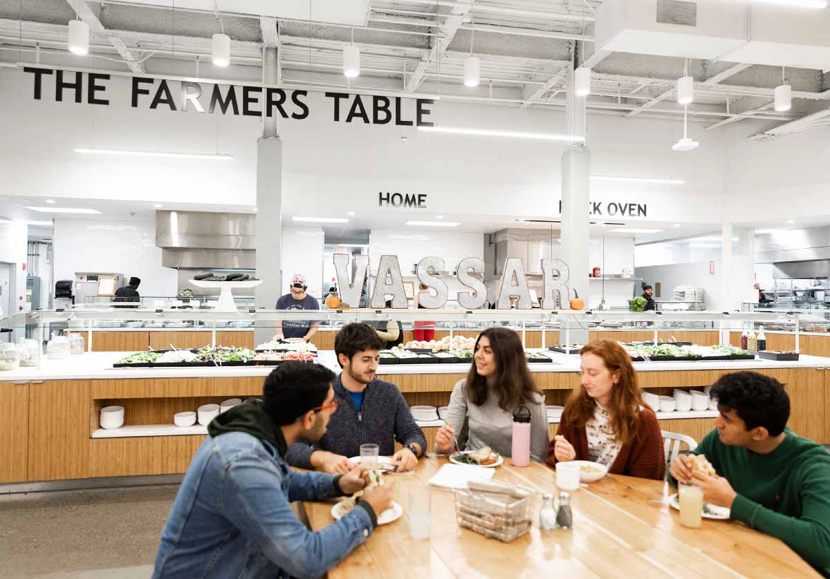 A group of five people sitting at a table eating and conversing in the Gordon Commons dining hall