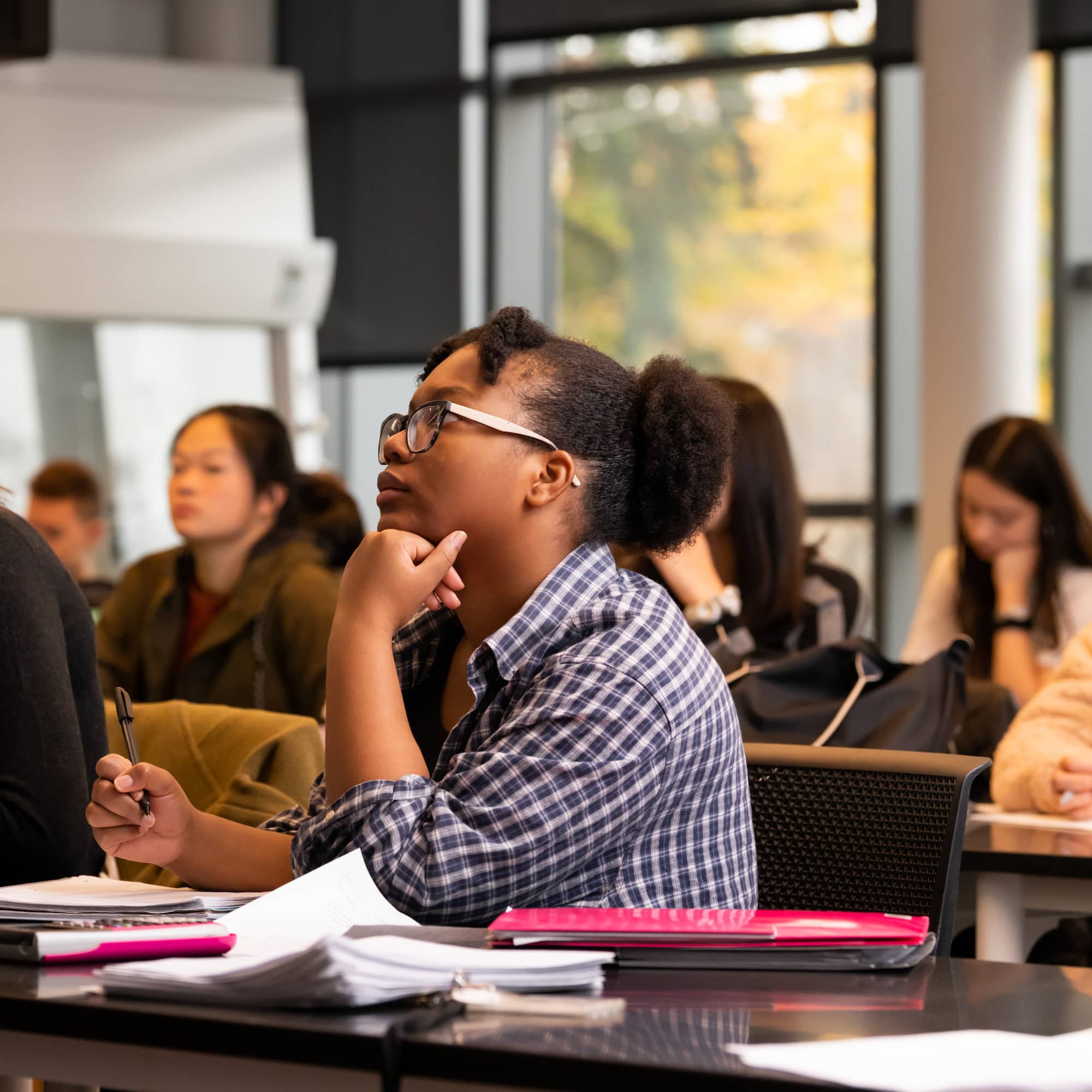 A photo taken from the side, showing a student sitting in a classroom with other students, looking straight ahead.