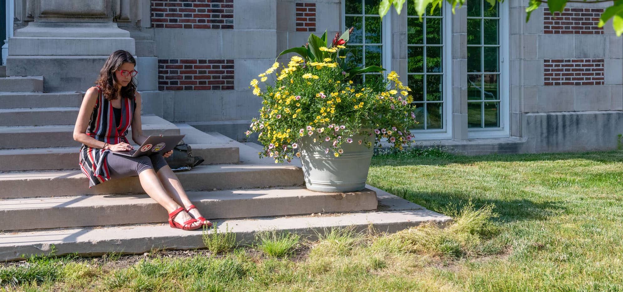 A person sitting on the steps using a laptop outside Rockefeller Hall