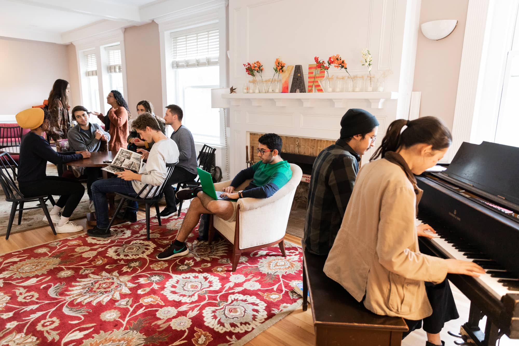 Students visting, reading, and playing piano in a residential common area