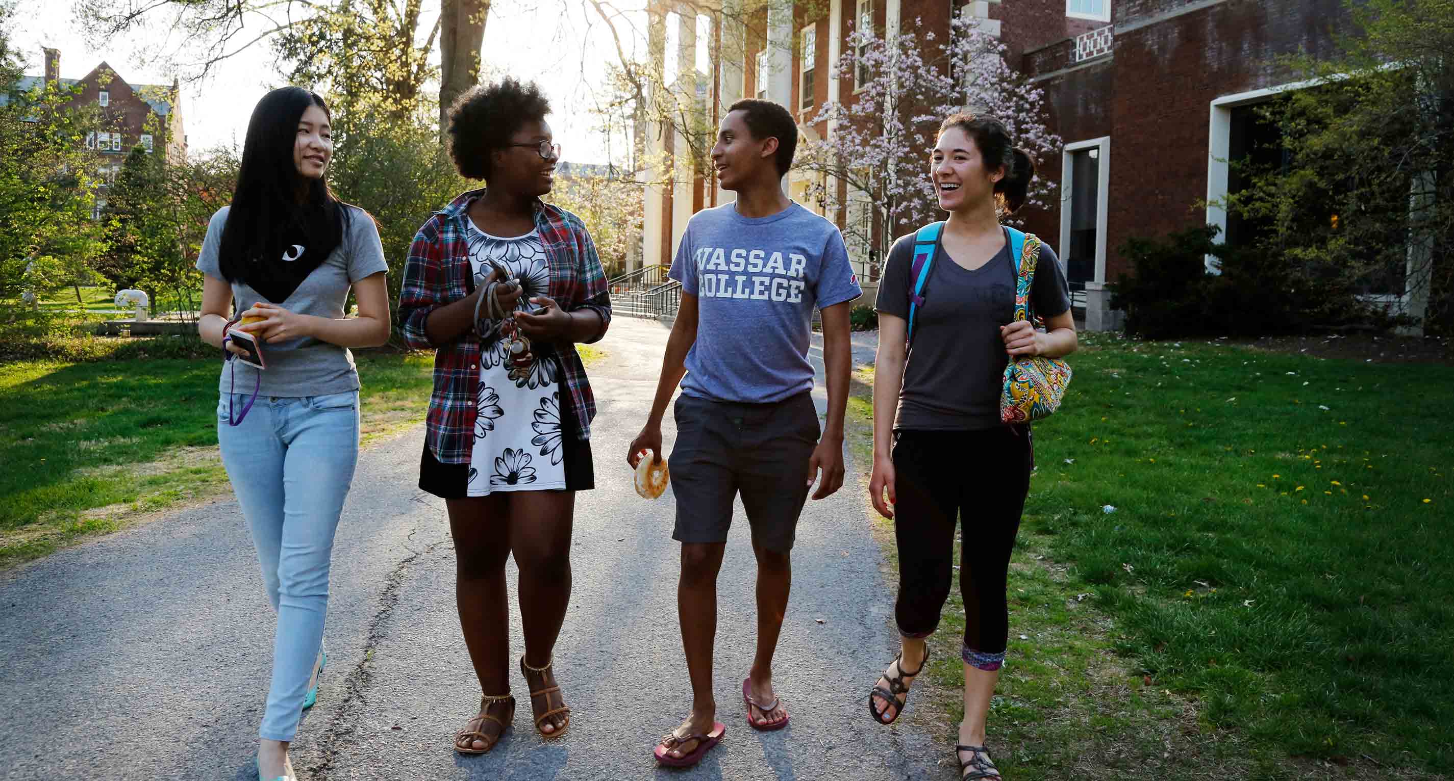 Four students walk past a large brick building, Vassar’s Gordon Commons, in the late afternoon