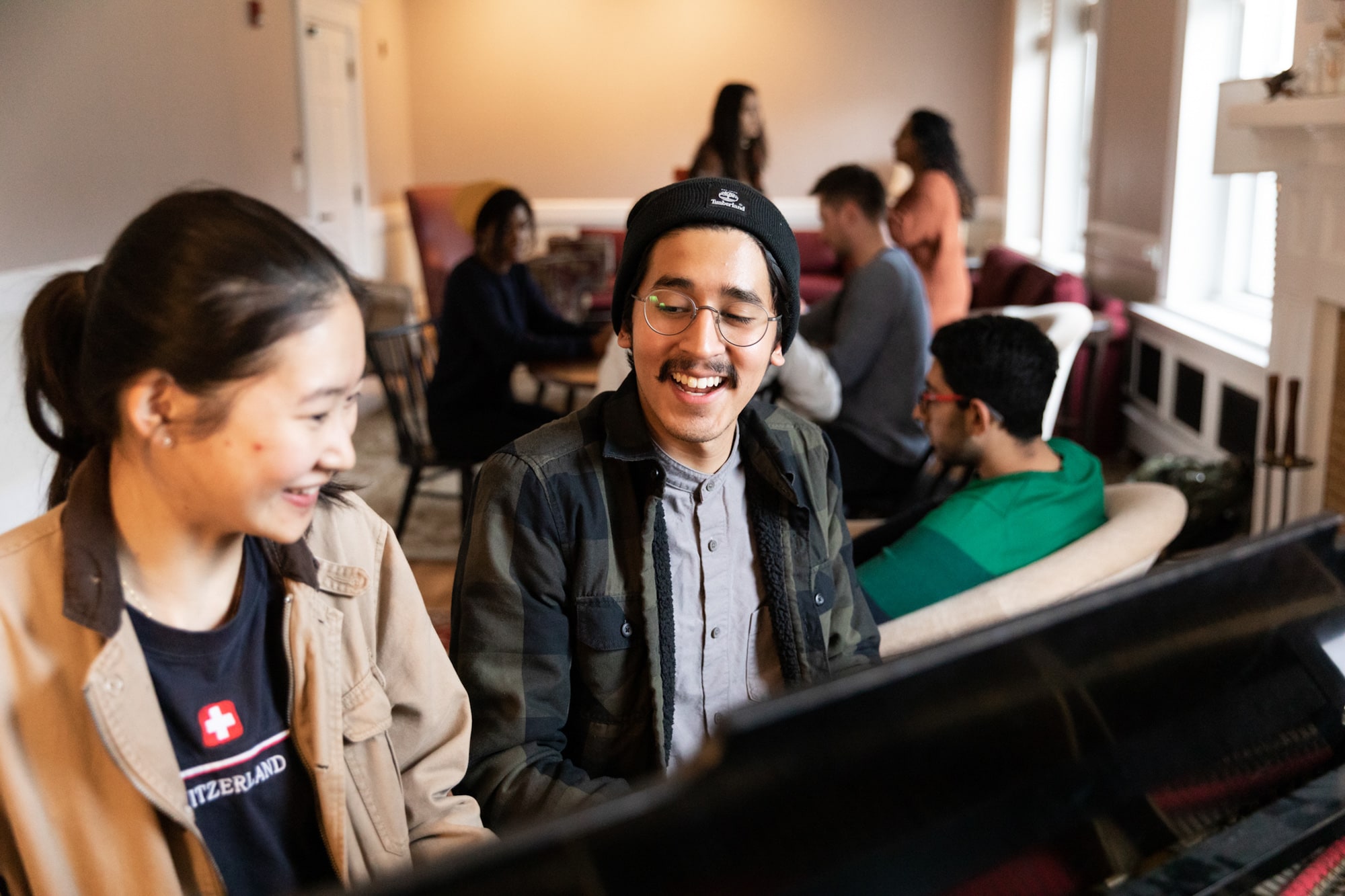 Two students play a piano in one of the common areas