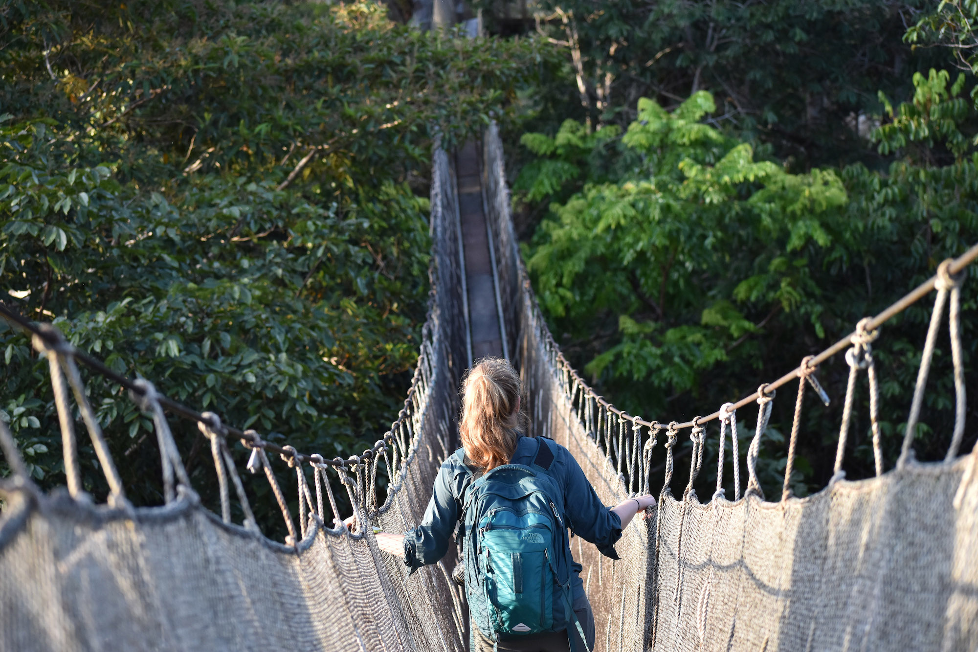 A student talking down a rope and cloth bridge in Peru