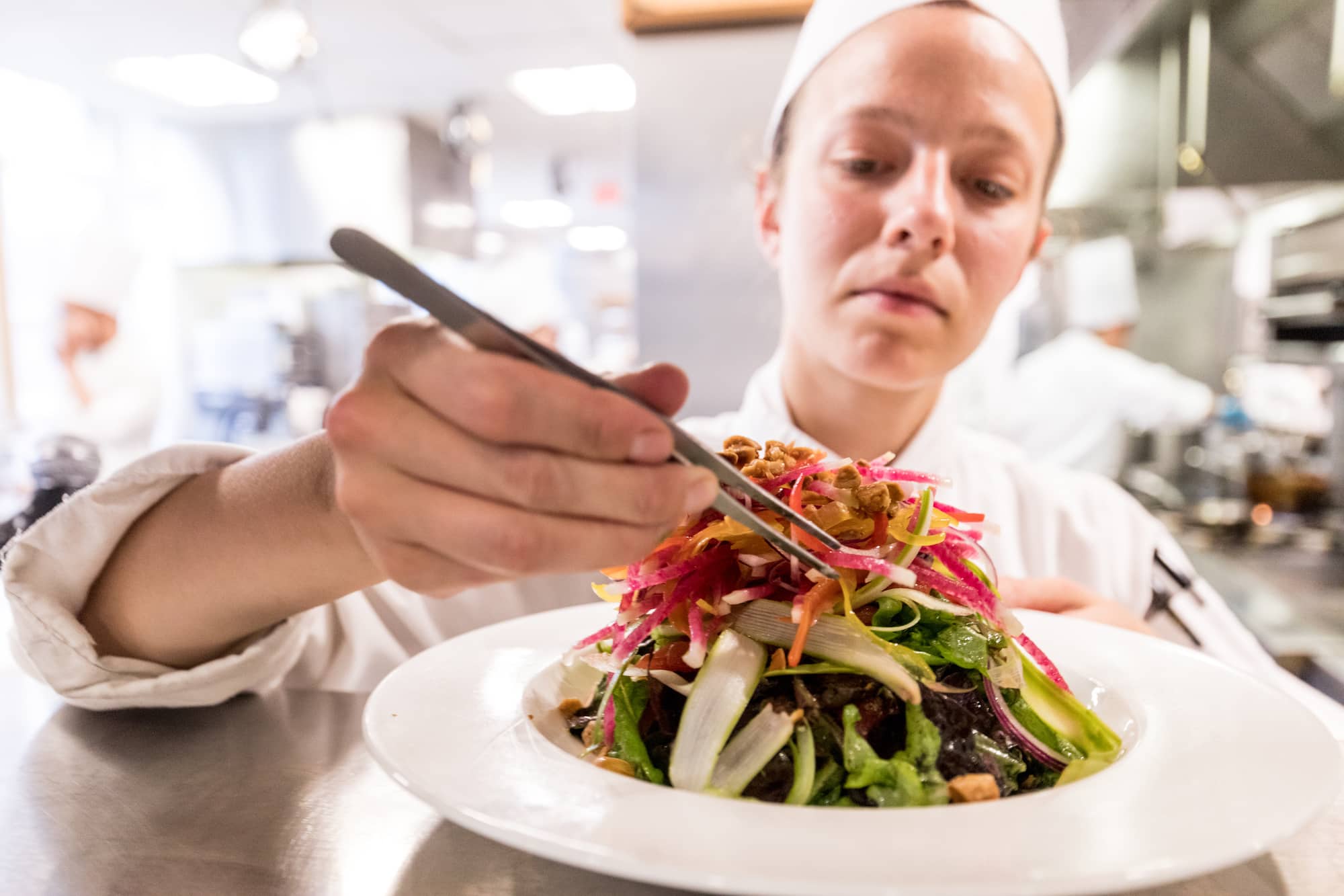 A person wearing white cooking clothes carefully assembles a fancy salad.