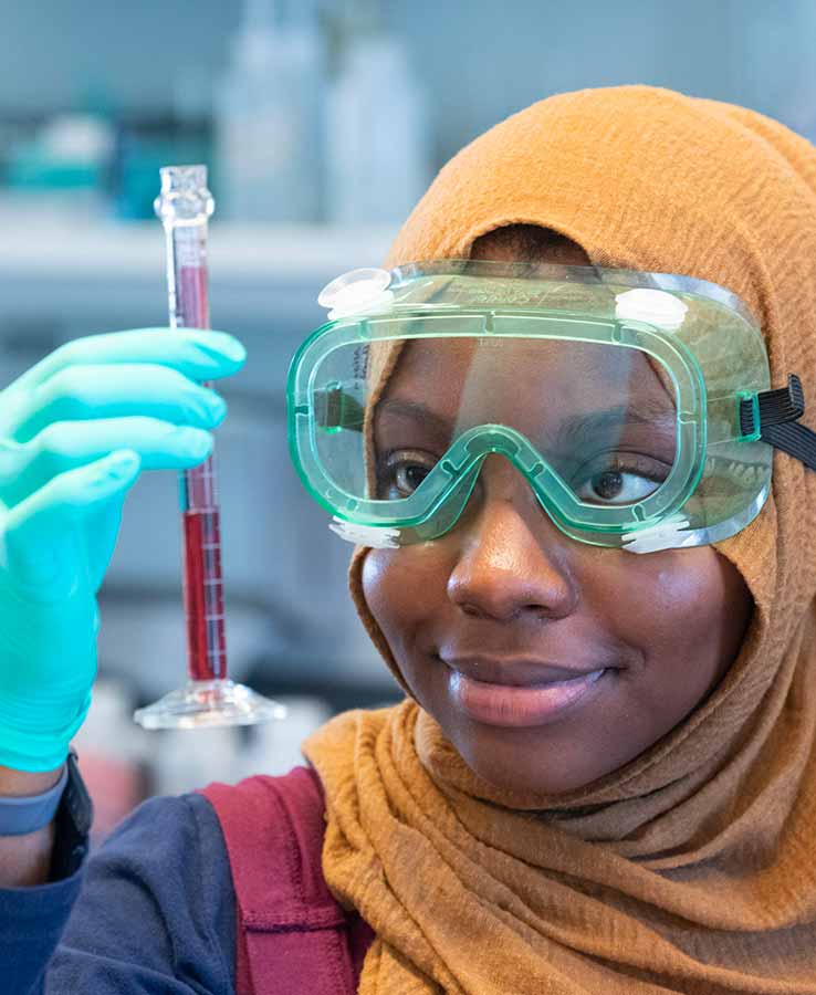 A student wearing goggles looks at a test tube