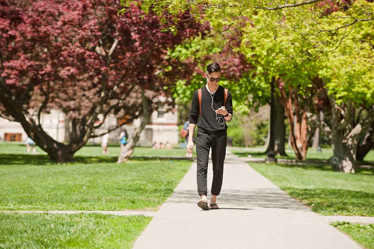 Student walking and looking at phone with ear buds