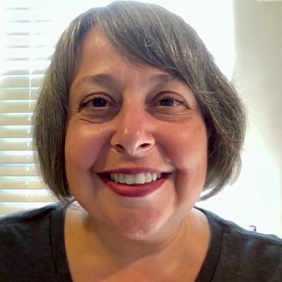 A person with short dark gray hair smiles at the camera.