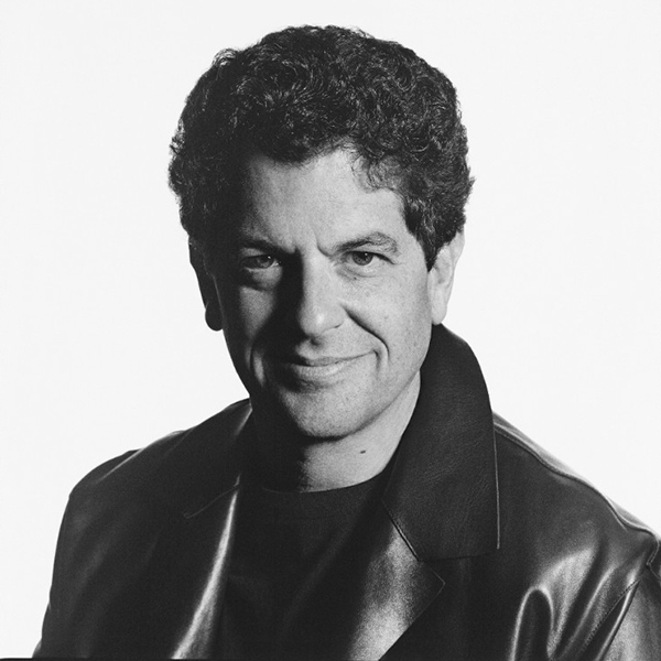 A person with short curly dark hair wearing a leather jacket smiles at the viewer.