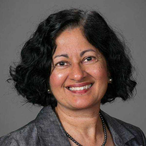 Jyotsna Vaid, a smiling person with short curly black hair, wearing a dark blazer and pearl earrings.