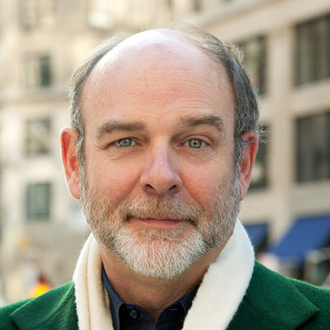 Paco Underhill, a gentle-looking person with a graying beard and bald head, wearing a green jacket and white scarf.