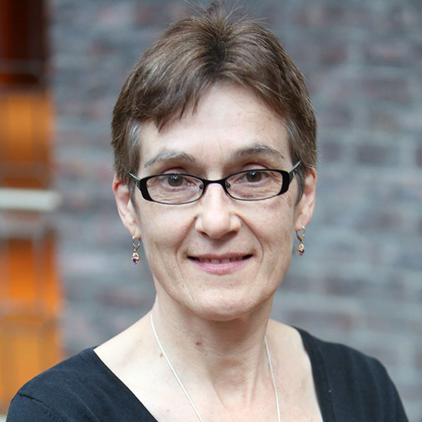 Marianne Begemann, a calm-looking person with short brown hair and glasses, wearing drop earrings and a black top.