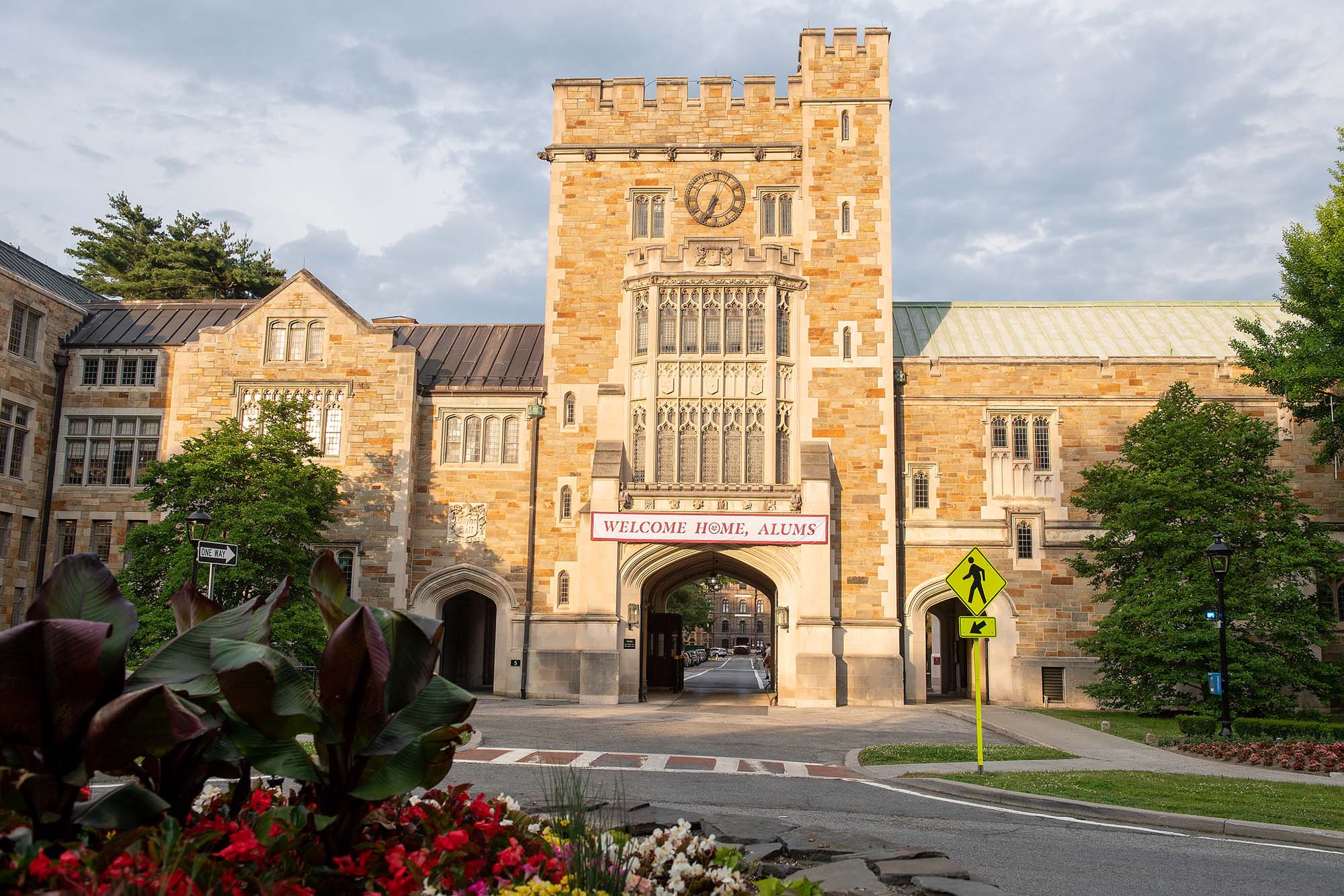 The Main Gate entrance to Vassar College, a large brick building with a tower over an archway wide enough for a vehicle, surrounded by greenery, in the late afternoon sunlight.