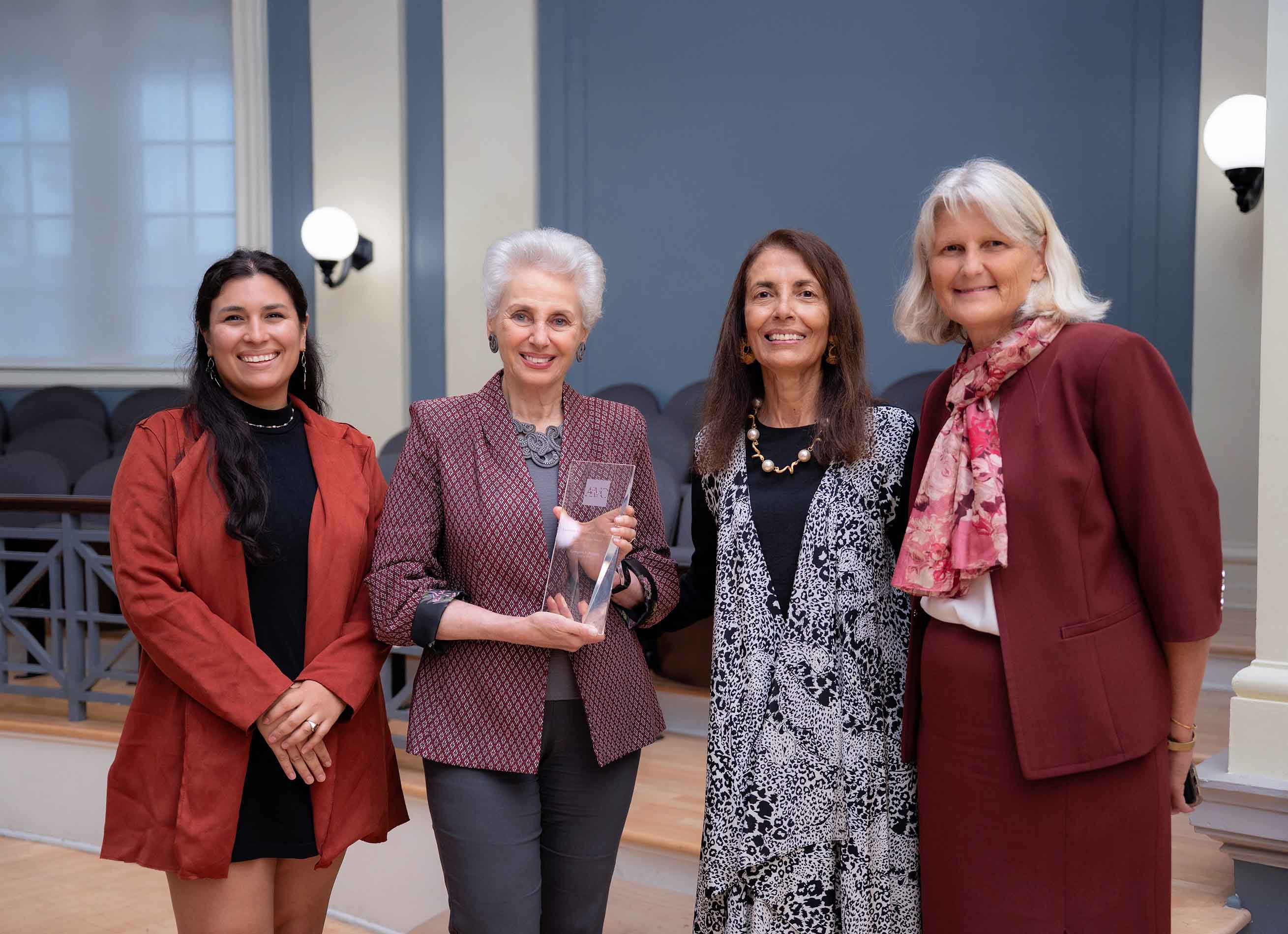 Four people standing together indoors, one holding an award, smiling for a photo after a ceremony.