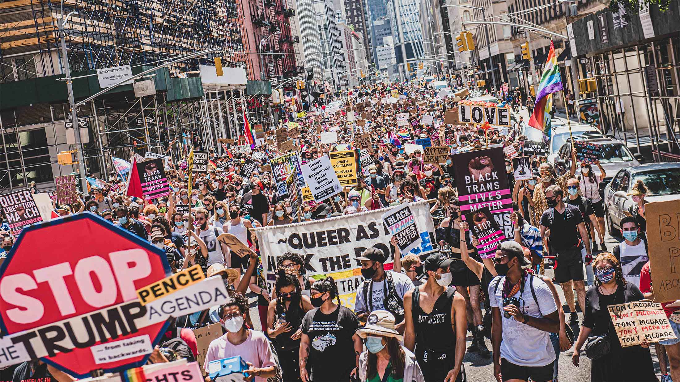 Crowds of people march down a city street holding various signs at the third annual queer liberation march in Bryant Park, NYC.