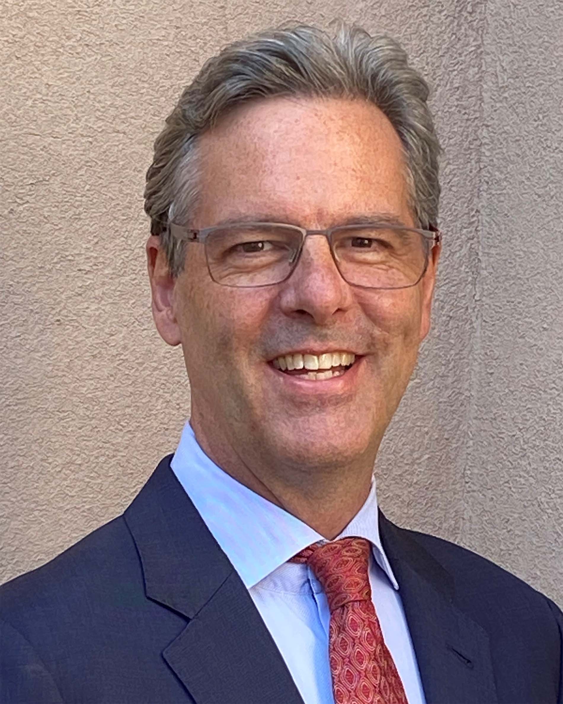 Russell Baker ’91, a smiling person with short hair in a suit and glasses.