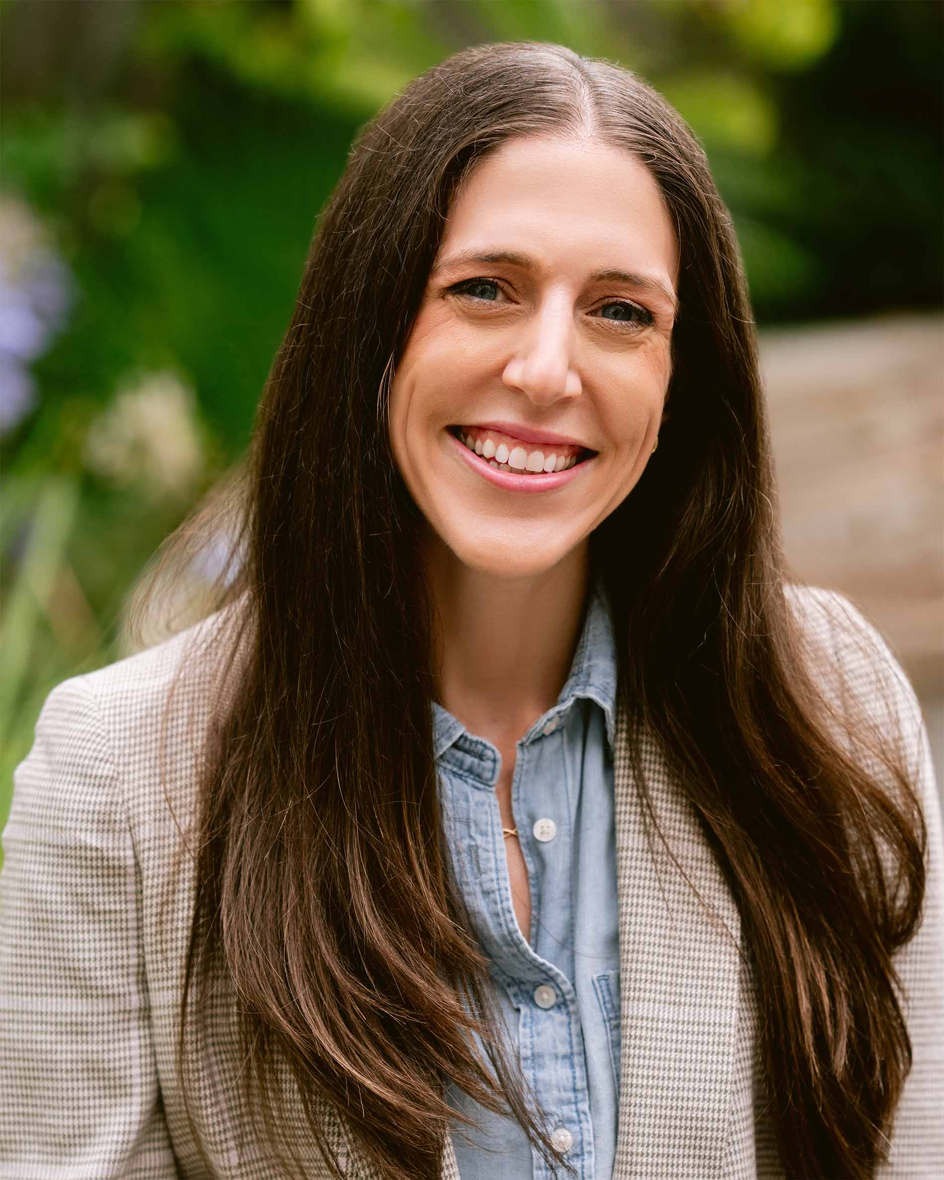 Alexandria Dempsey ’09, a smiling person outdoors with long brown hair, wearing a blazer and blue shirt.