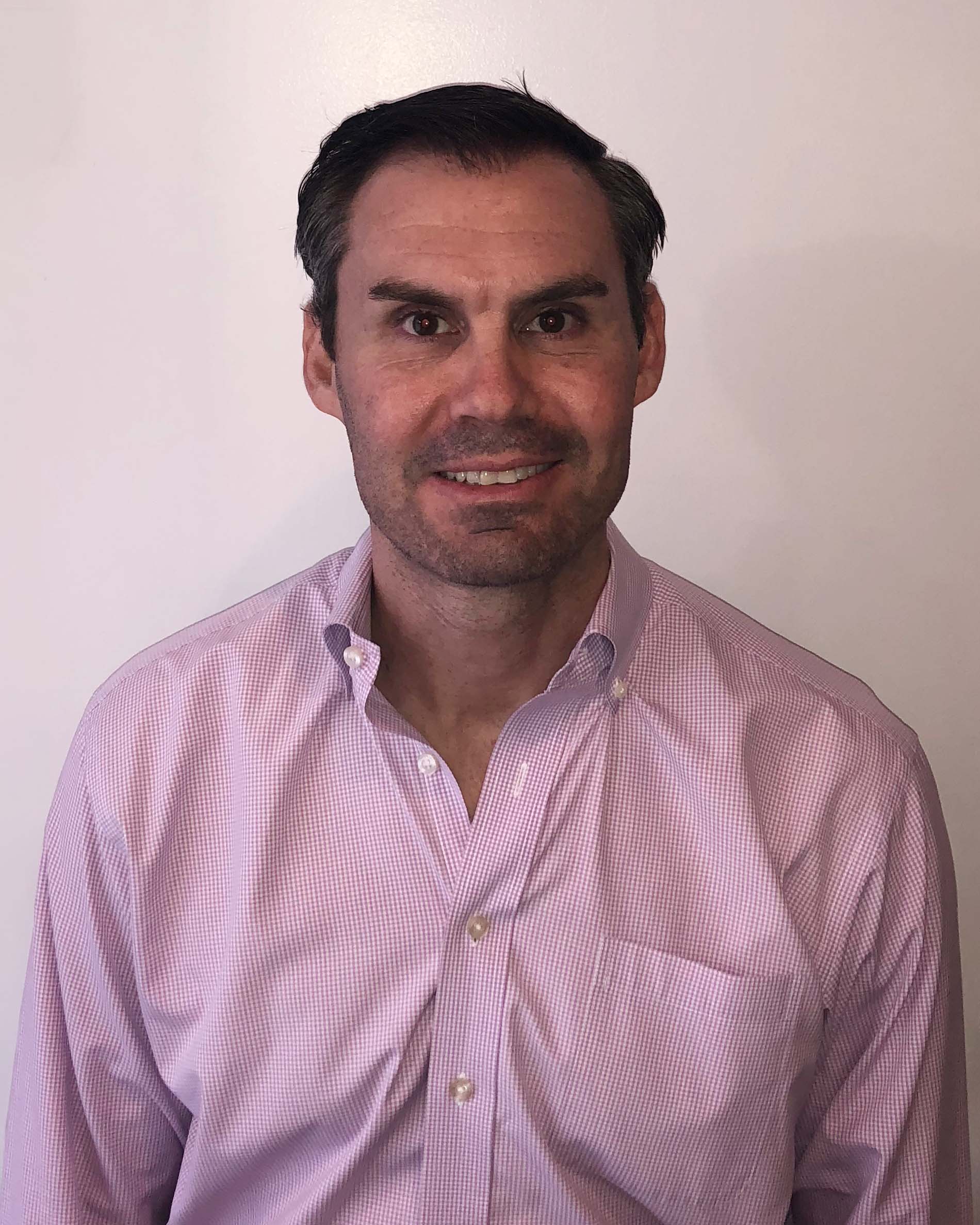 Christopher Deutsch ’97, a person in a pink button-down shirt smiling against a plain background.