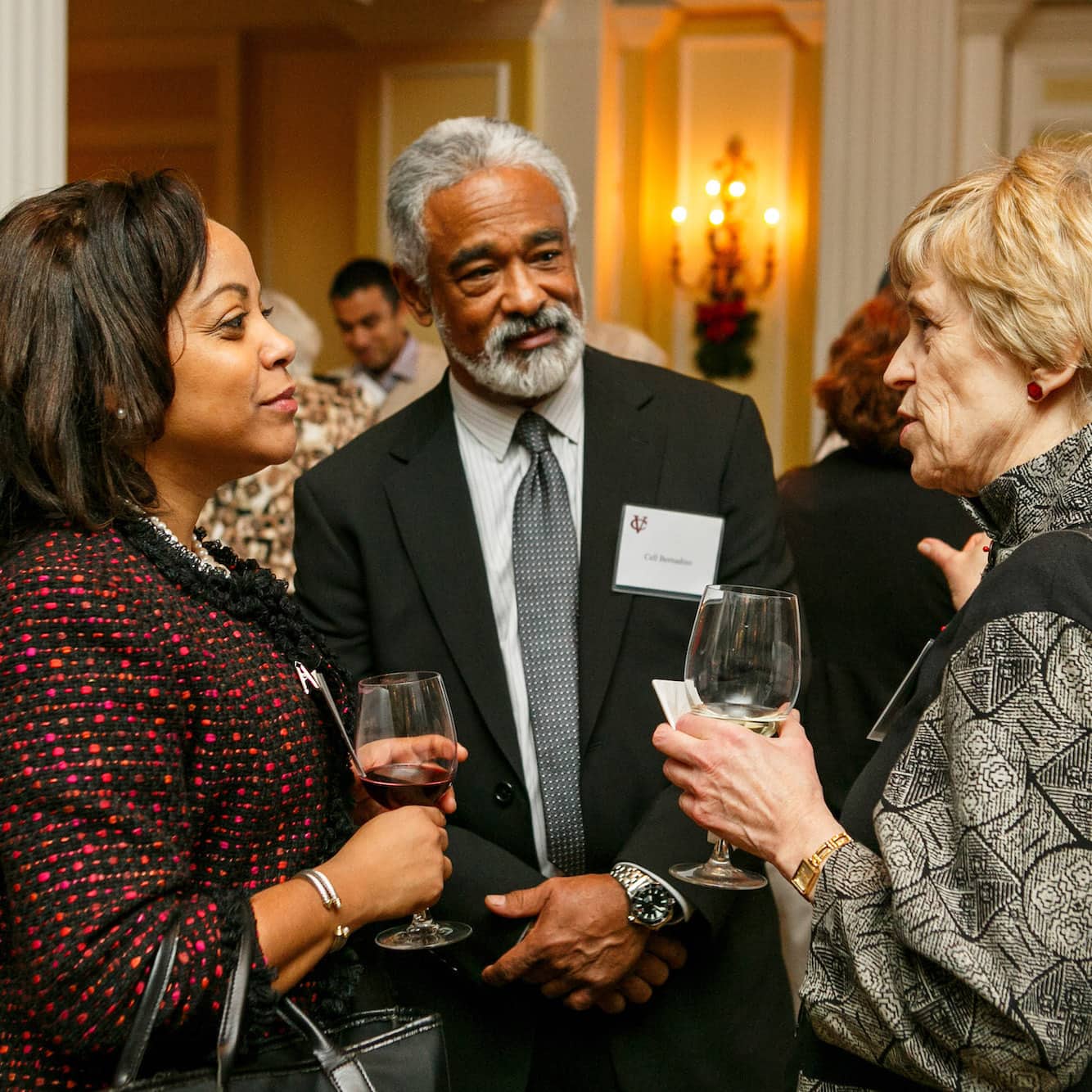  Three people stand in a circle speaking to each other, wearing formal attire.