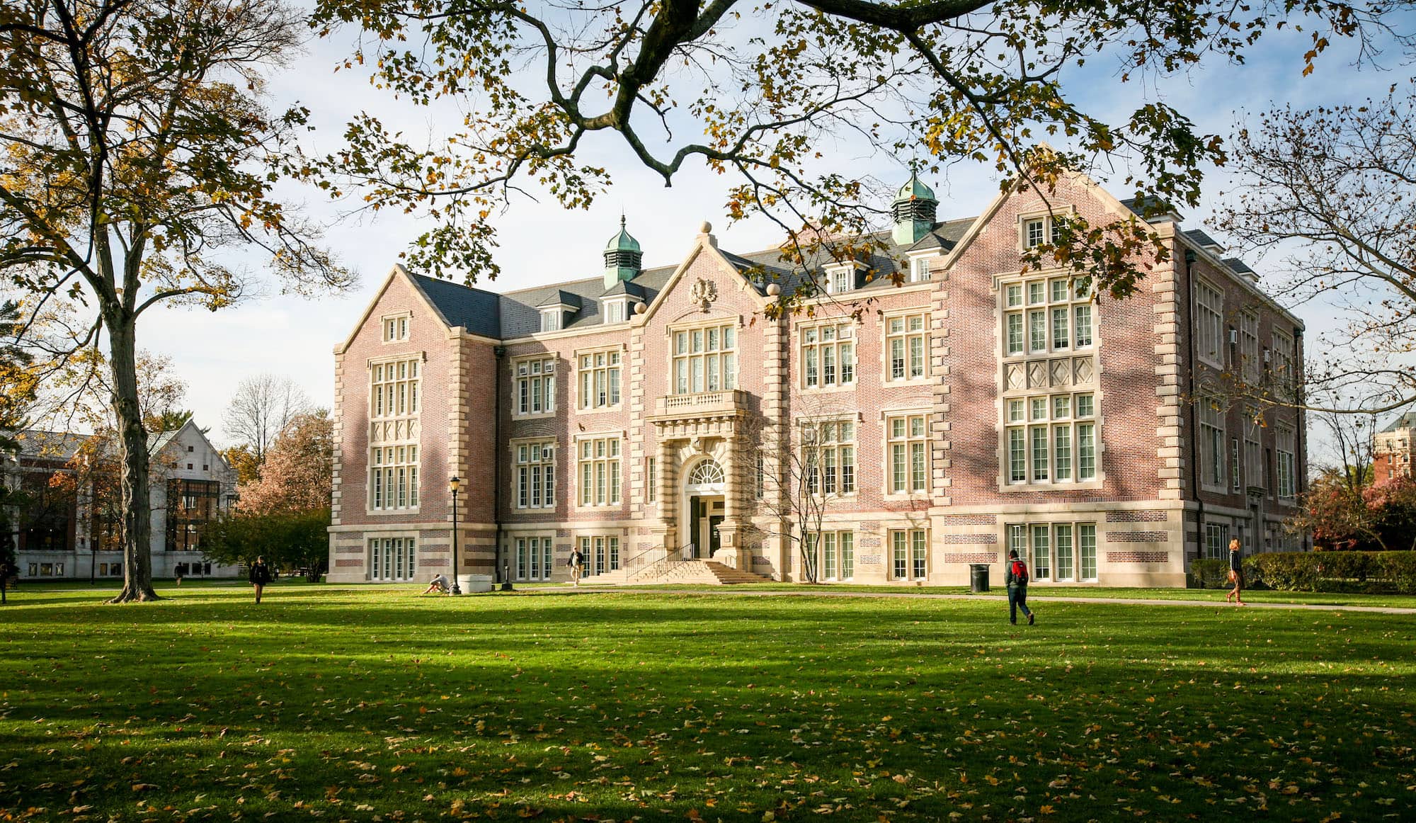 Rockefeller Hall, a large brick building on Vassar’s campus, with several large windows surrounded by various trees on a clear day.