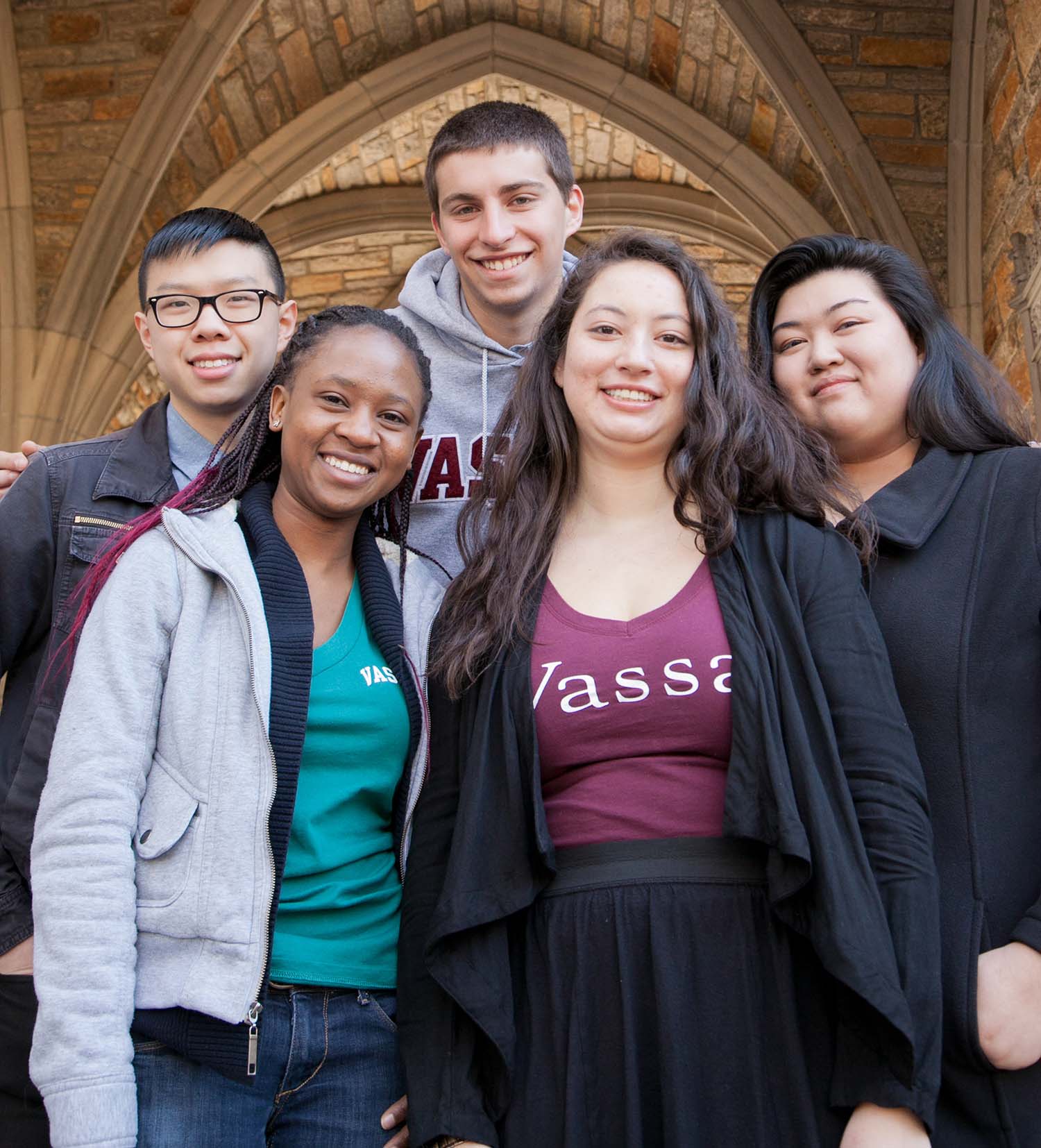 Five students under an arched ceiling smiling at the camera.