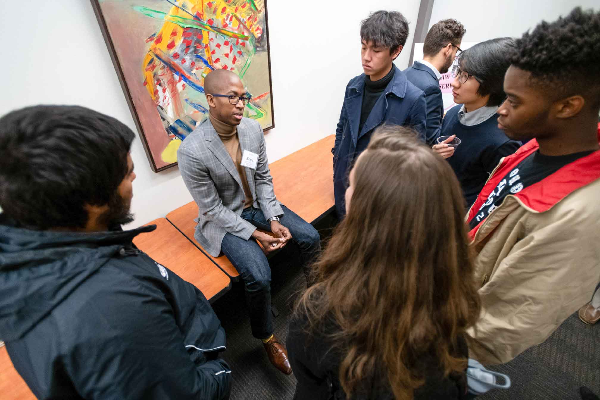 Seated person in front of a painting addressing a standing group.