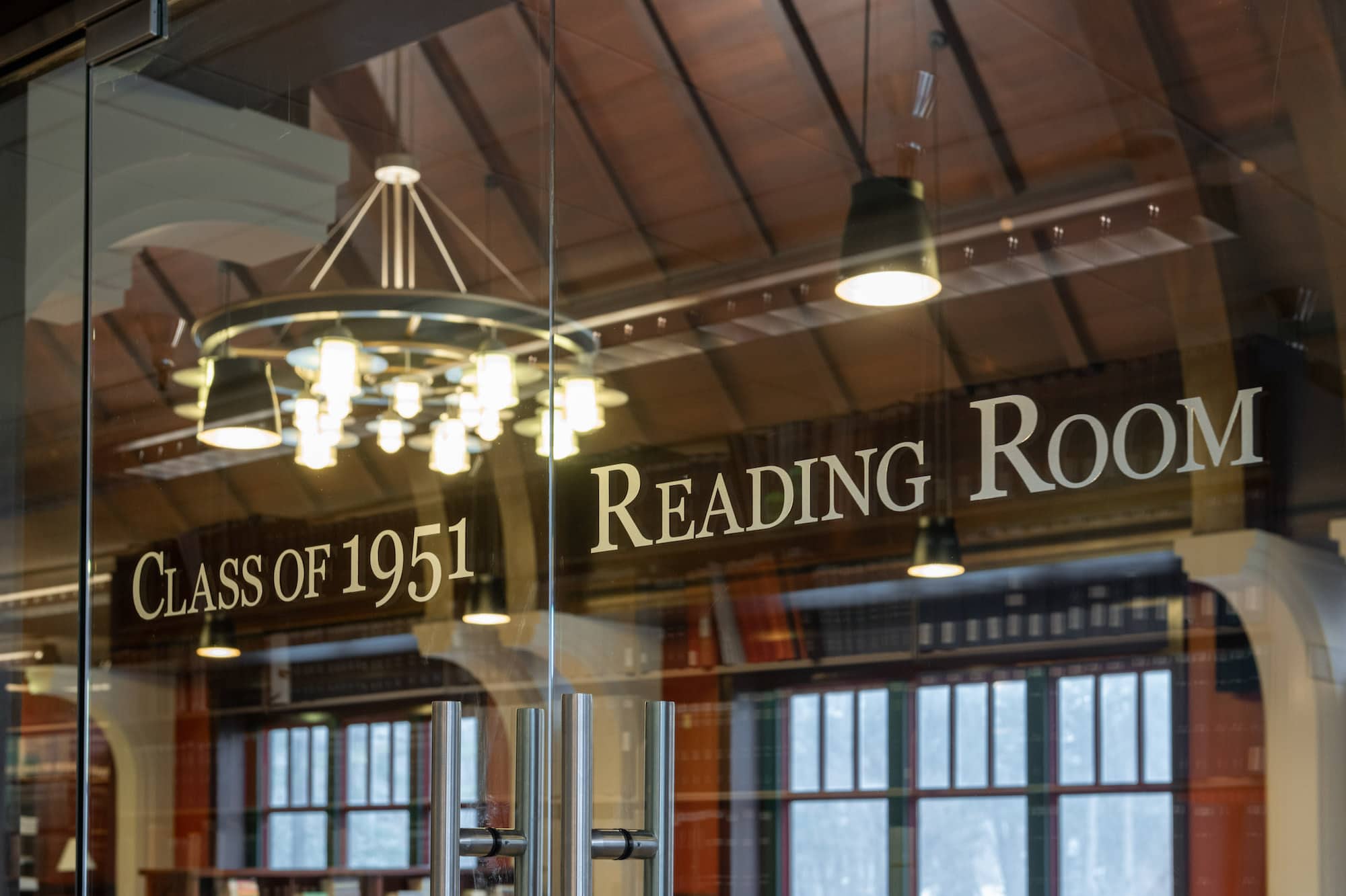 Interior view a room with a sign that reads Class of 1951 Reading Room in a black frame with large windows below it.