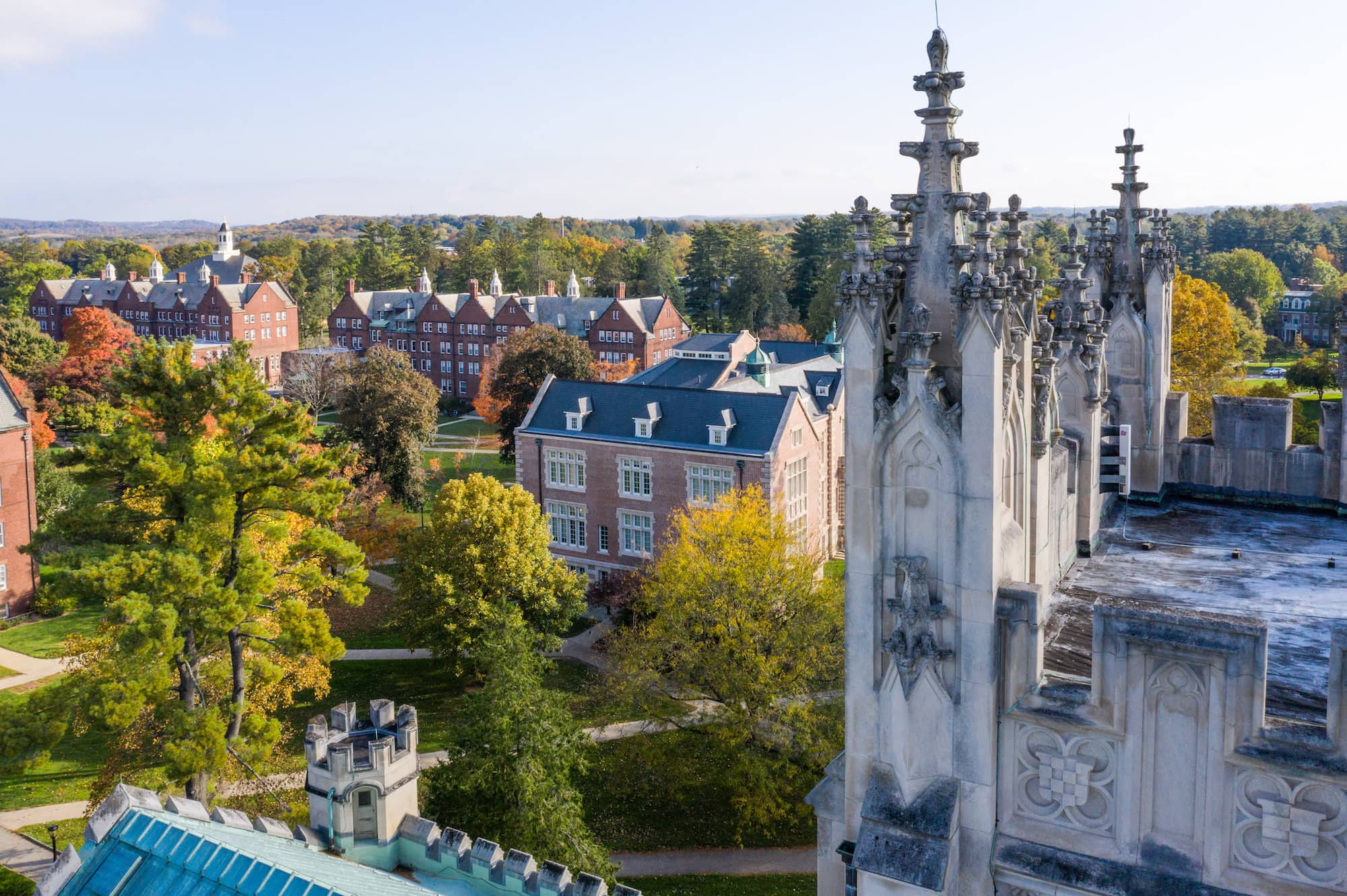 An aerial view of various large buildings on Vassar Campus, one with towers made of marble on the right, and a group of brick buildings in a quadrangle on the left, all surrounded by trees. 
