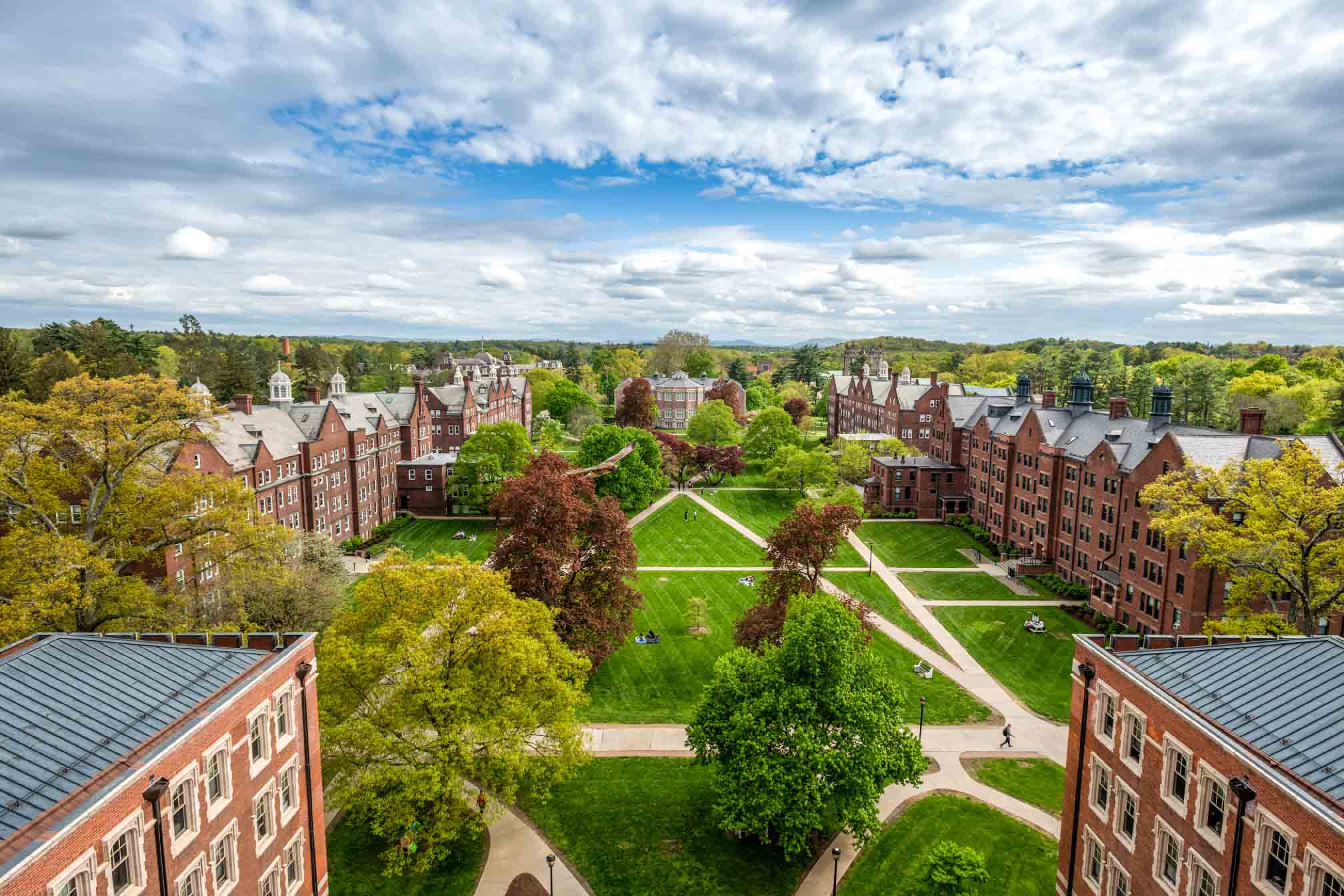 Aerial view of the Vassar campus residential quad featuring traditional red brick buildings with white trimmings,  lush green lawns, and concrete paths crisscrossing the lawns, leading to various buildings.