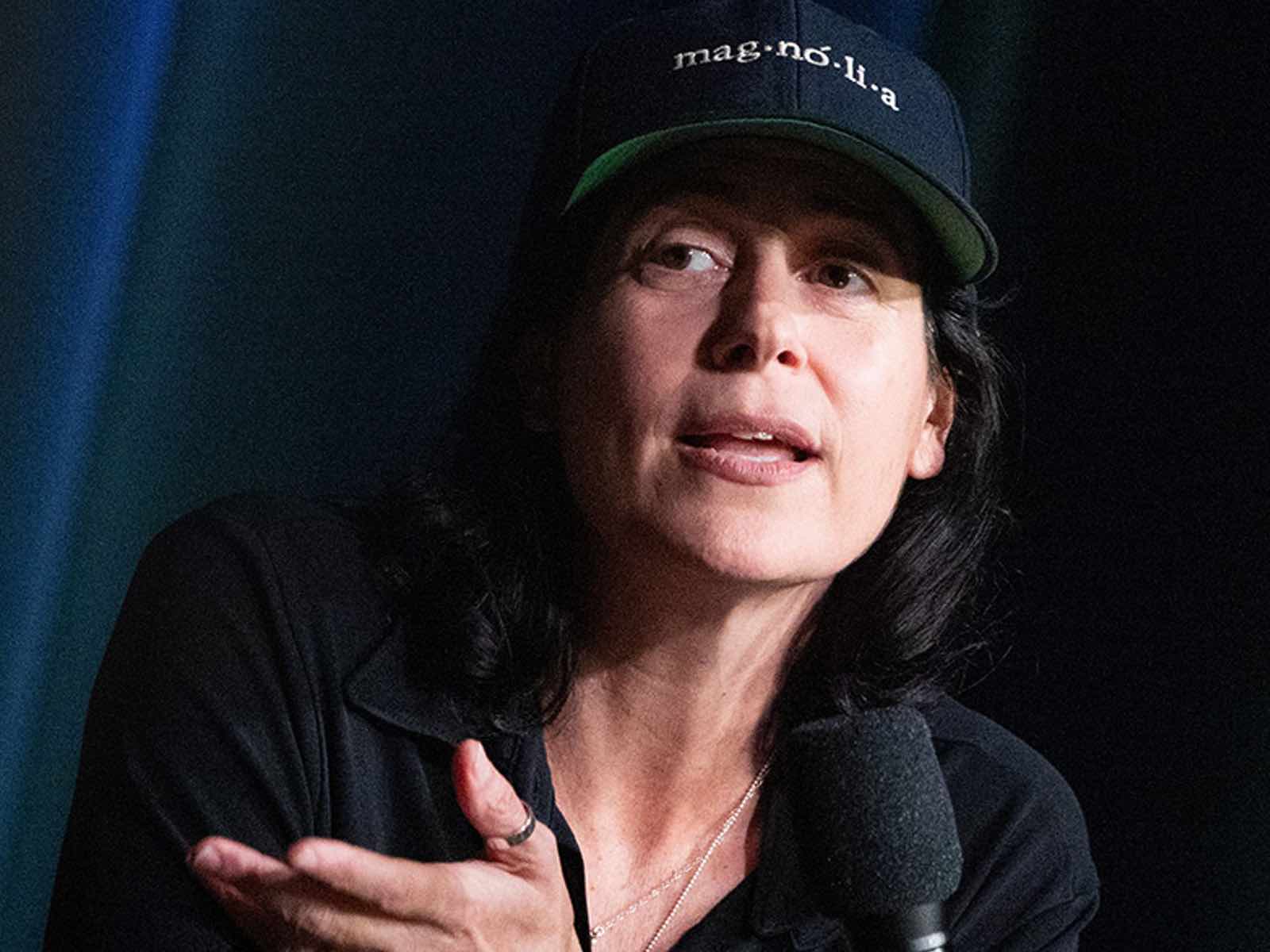 Cassandra Kulukundis ’93, a person with long black hair, speaks while wearing a baseball cap with the word 