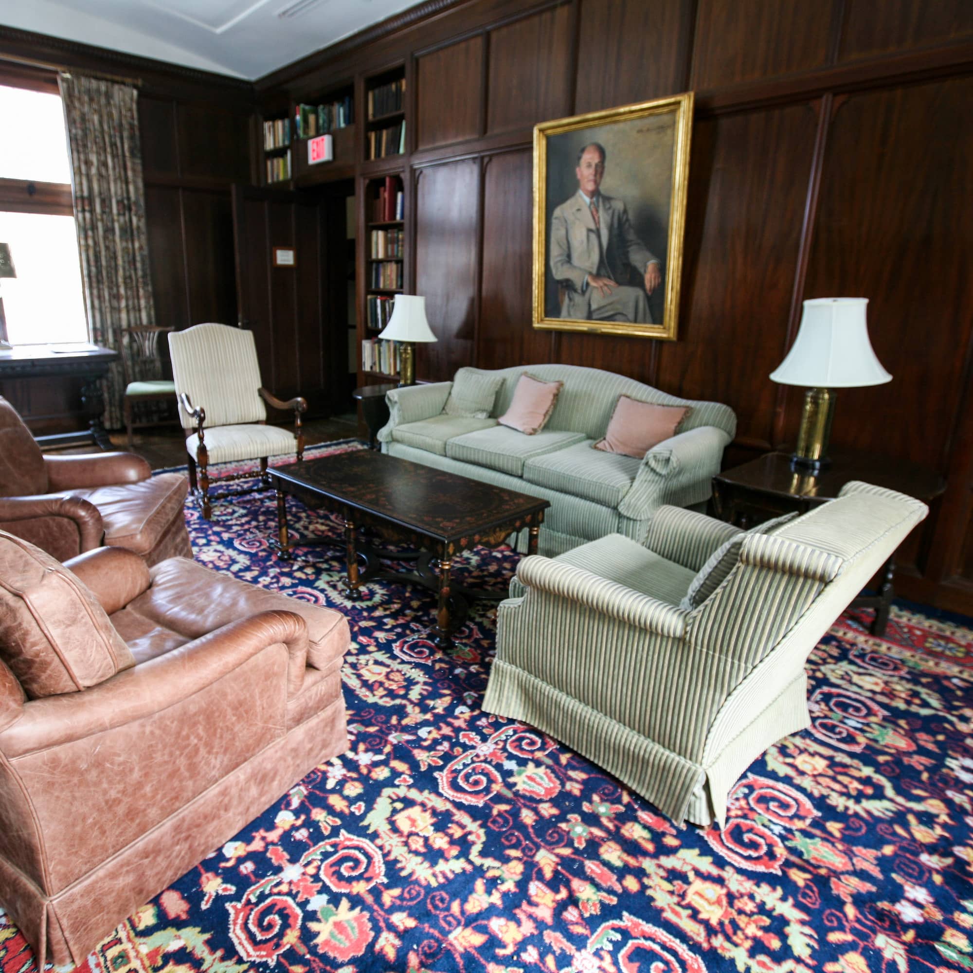 A medium-sized room with dark brown walls, a bright purple patterned rug and different chairs and couches arranged around a coffee table.