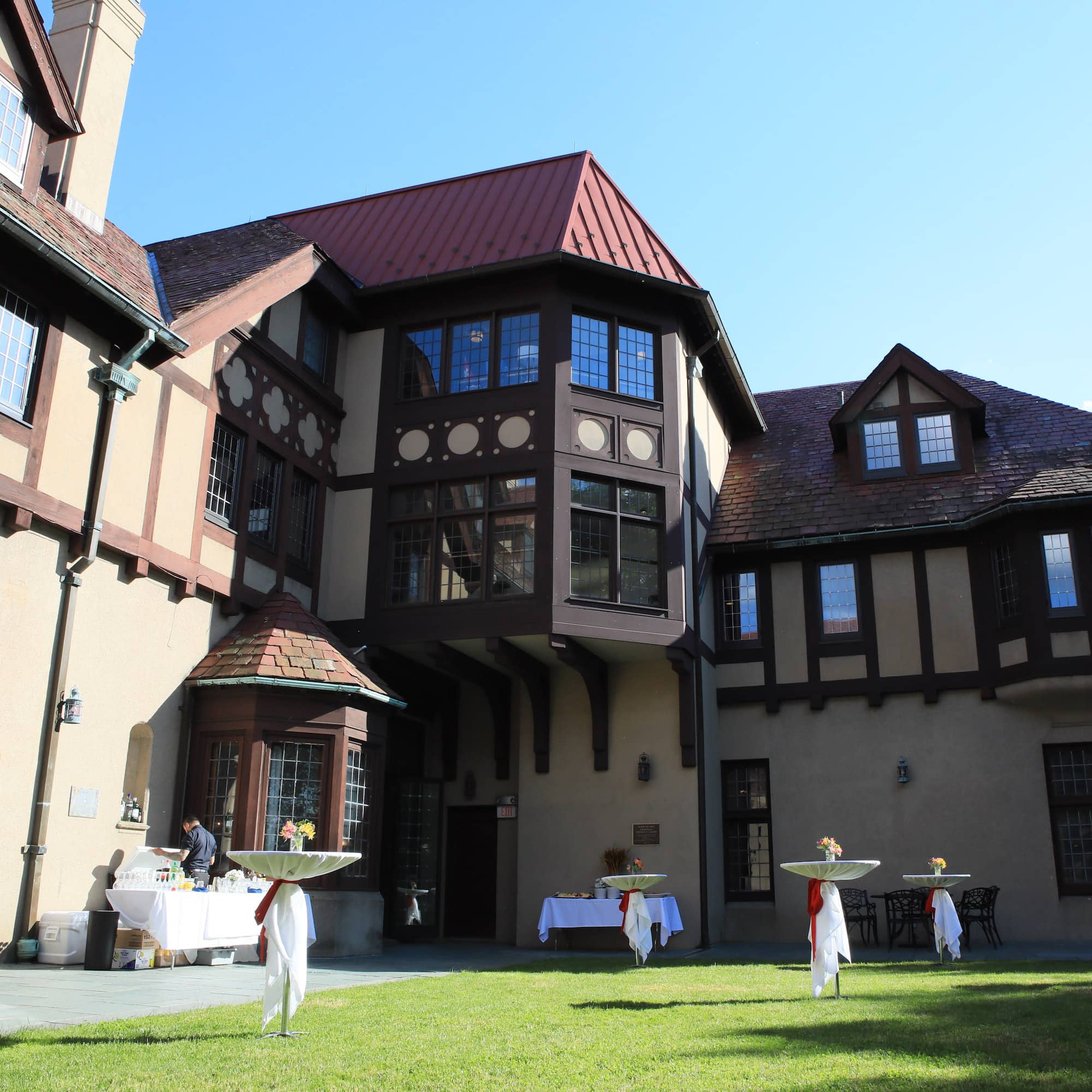 A green courtyard surrounded by a flagstone patio and the walls of a large beige building with a red roof and brown framing.