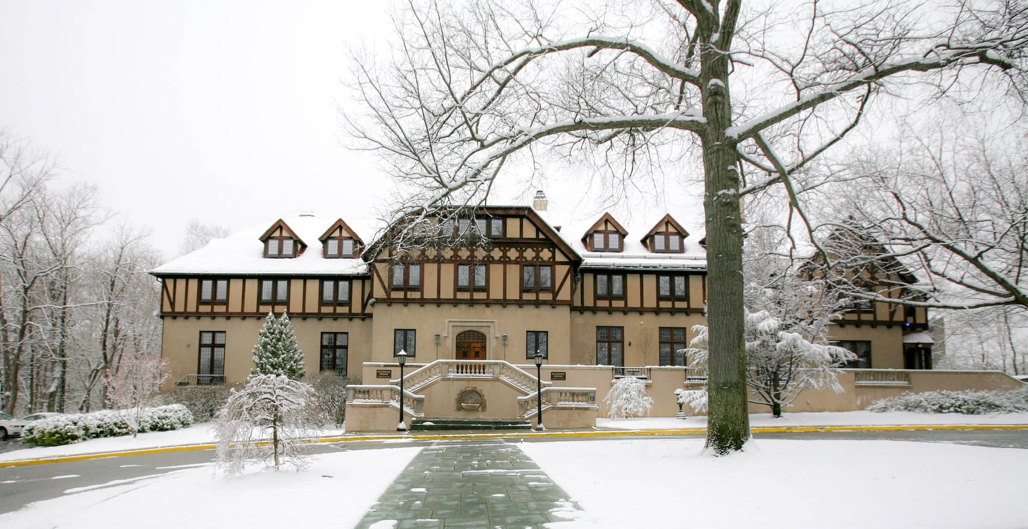 The front exterior of Alumnae House on the Vassar campus, a large beige building with a red roof and many windows across the entire building, covered in snow.