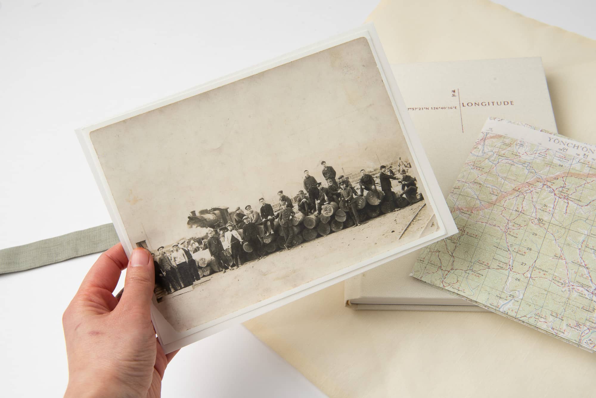 Hand holding a black and white photograph above a map and a book on a table.