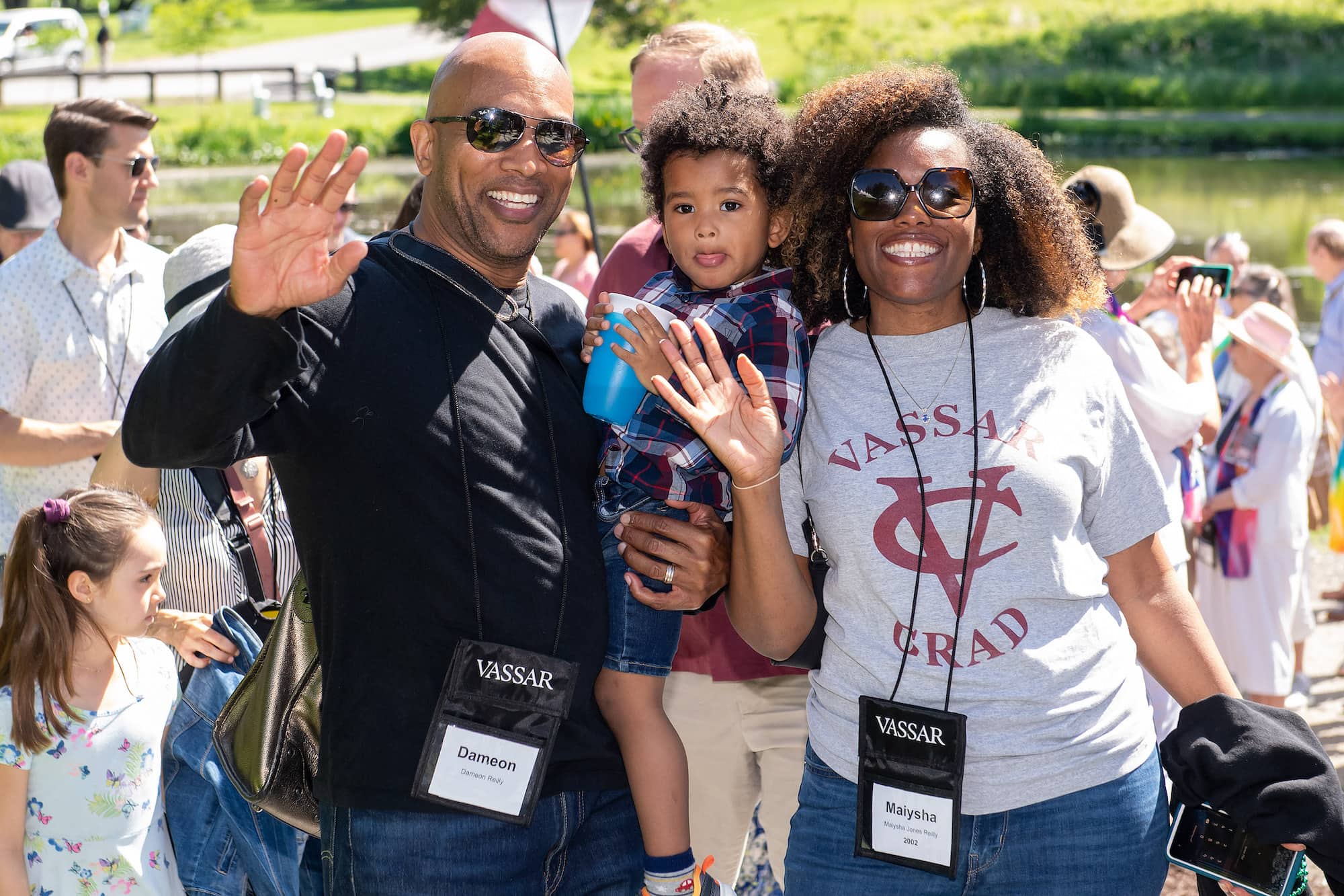 Two adults, one in a black sweater and jeans carrying a child and the other in a grey shirt that reads 