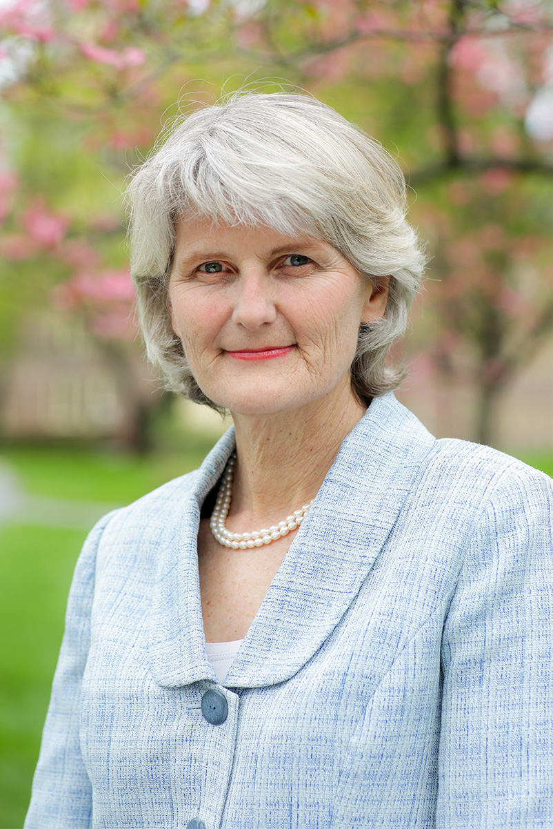 Elizabeth Howe Bradley wearing a light patterned jacket and pearl necklace with trees in the background.