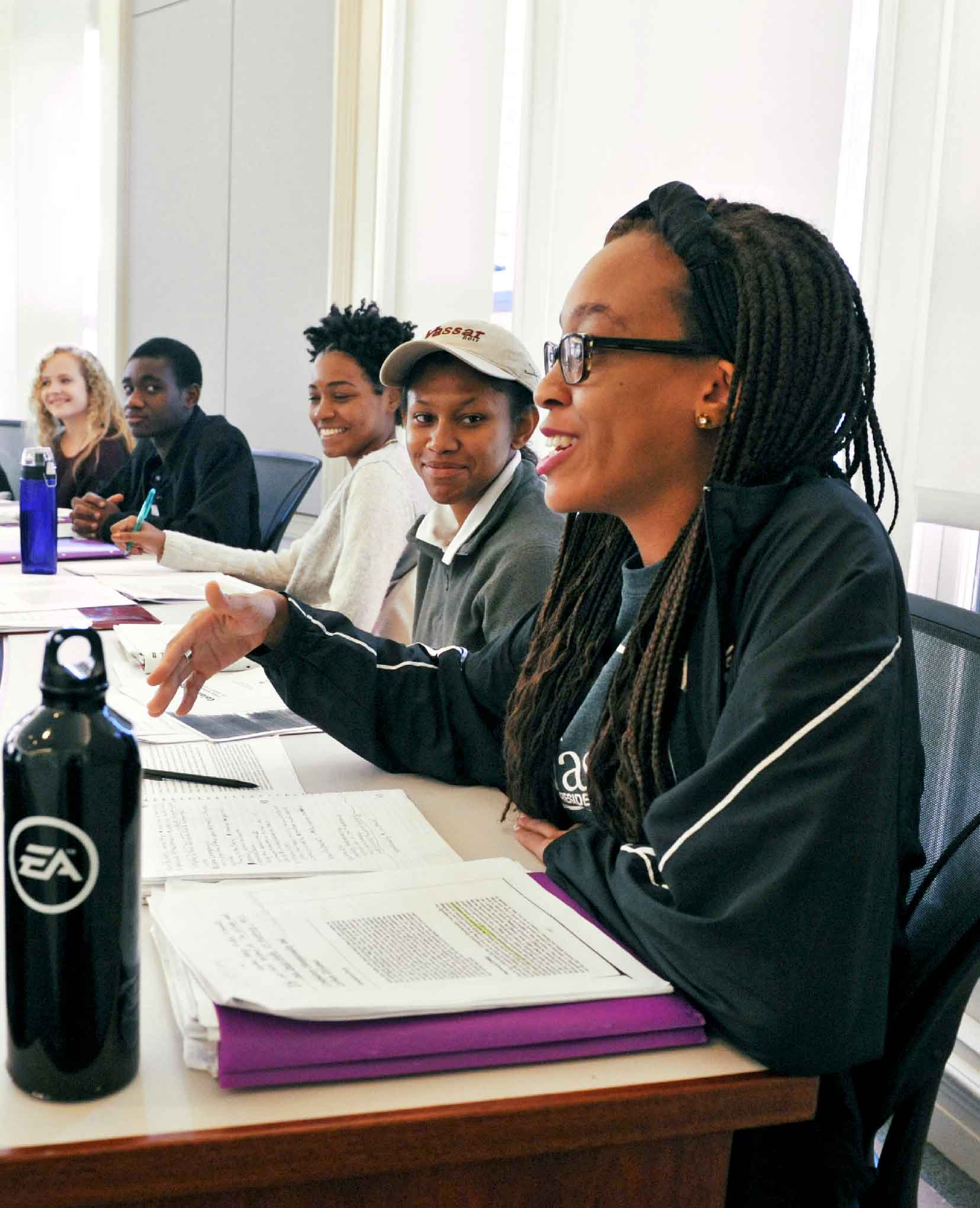 Professor and students sitting in a classroom, professor leading discussion.