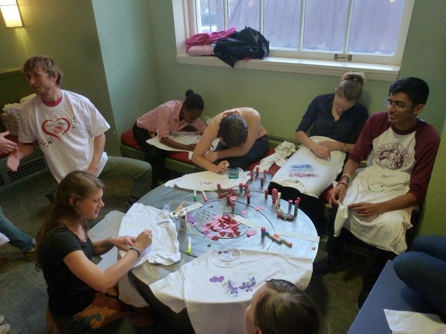 A group of students sit at a circular table, decorating T-shirts