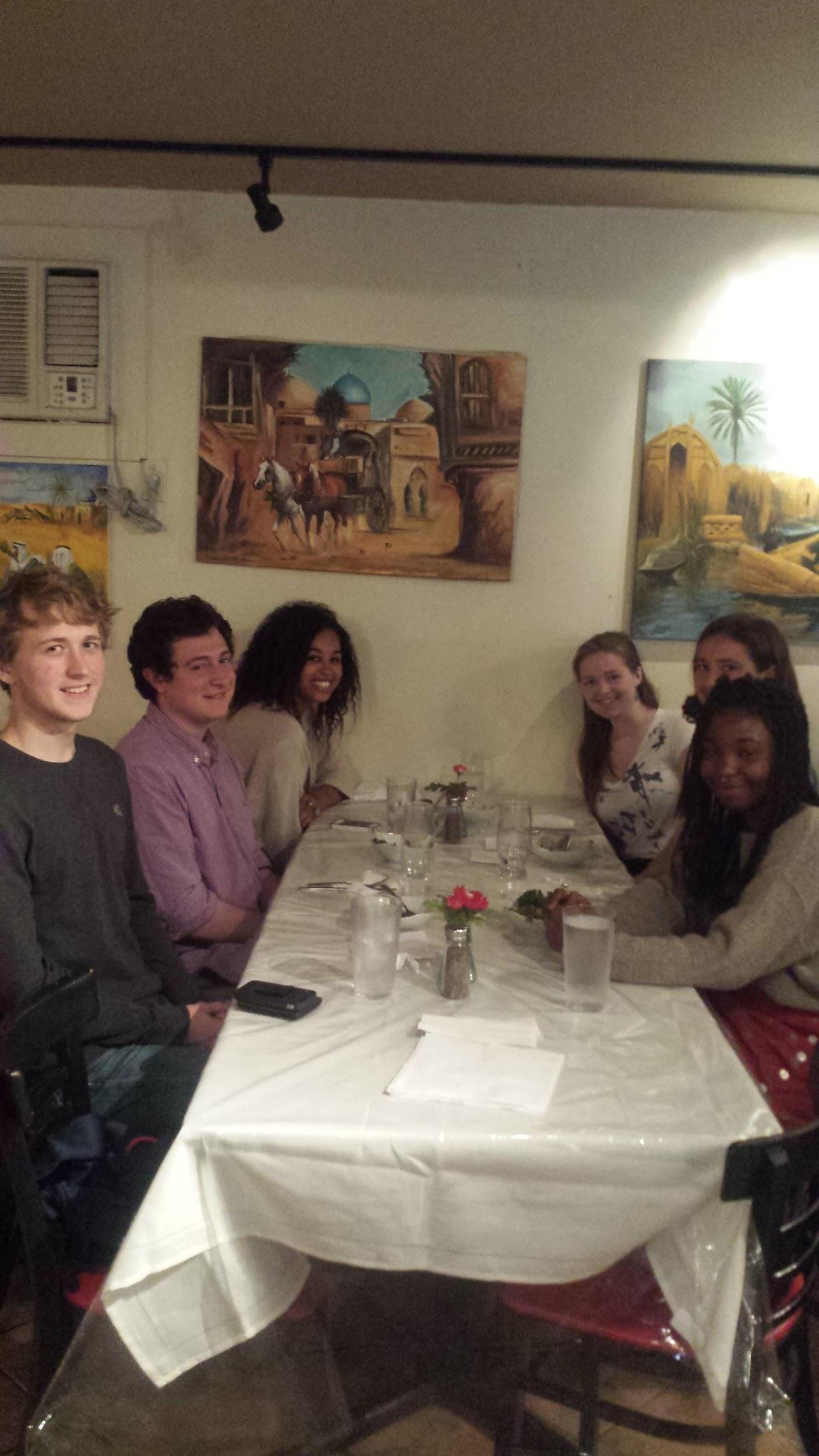 Six students sit at a restaurant table, smiling at the camera