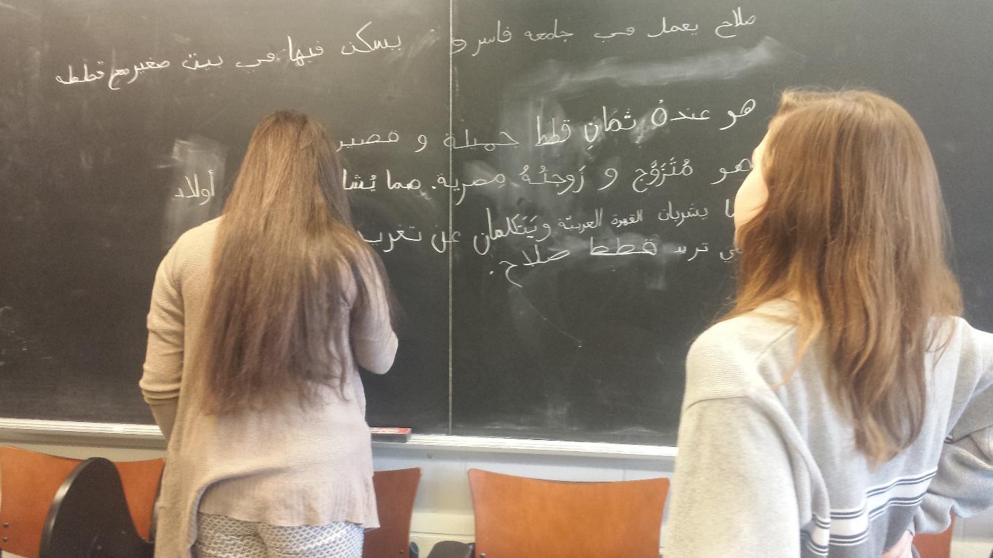One student watches another write on a blackboard
