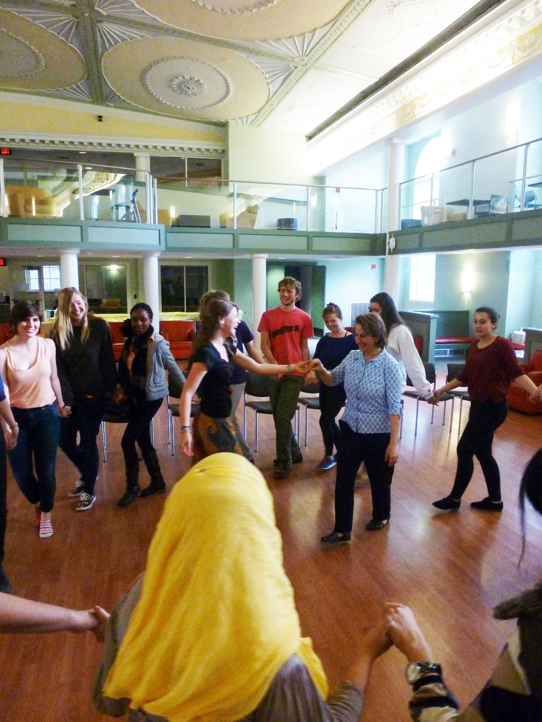 A group of students dance on a hardwood floor in a large, open room